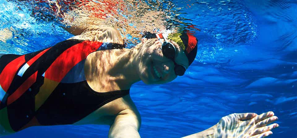 smiling woman wearing swimming cap and goggles swimming underwater